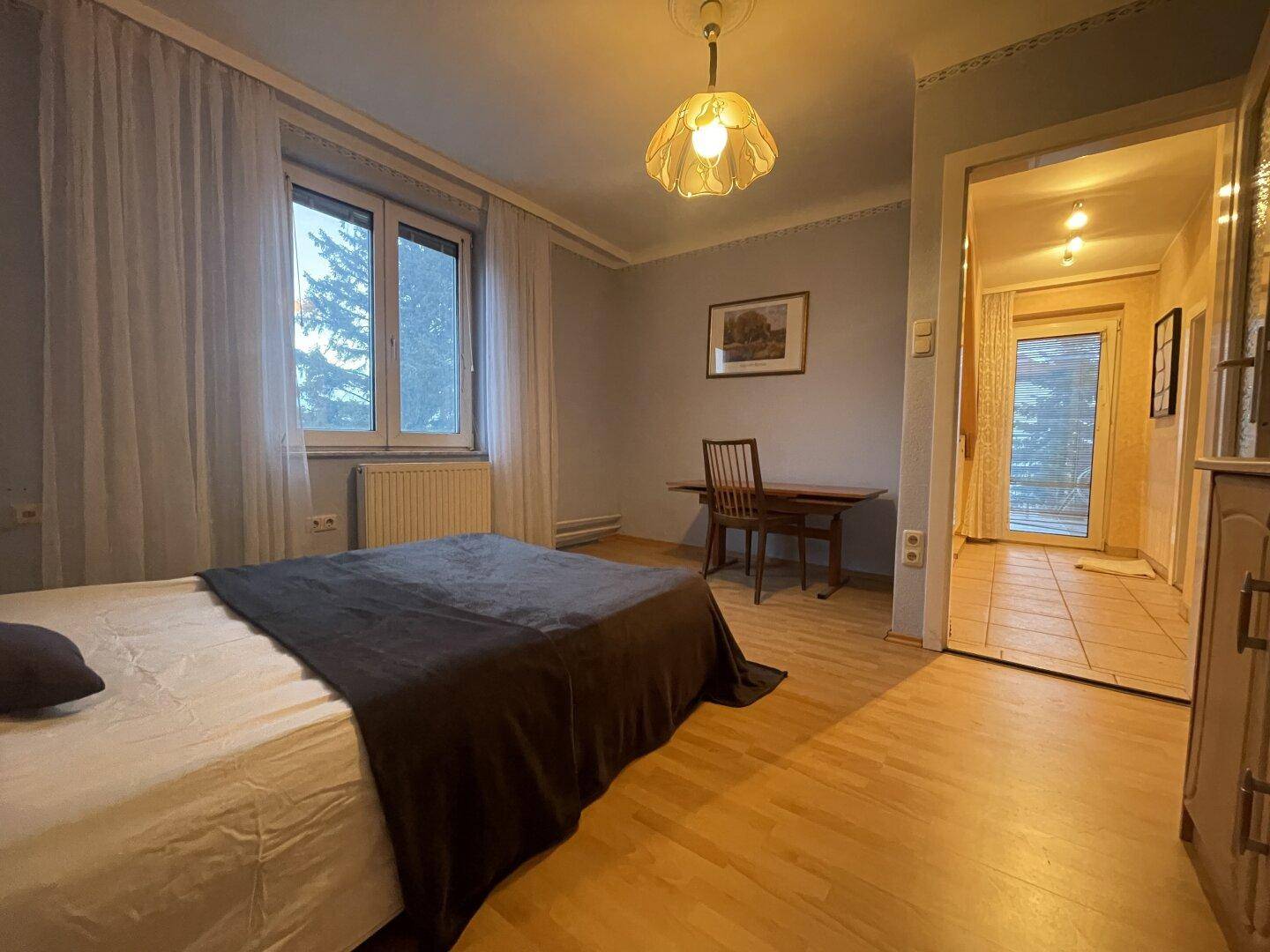 Schlafzimmer mit Parkettboden, Bett und Schreibtisch, mit Zugang zum Flur.