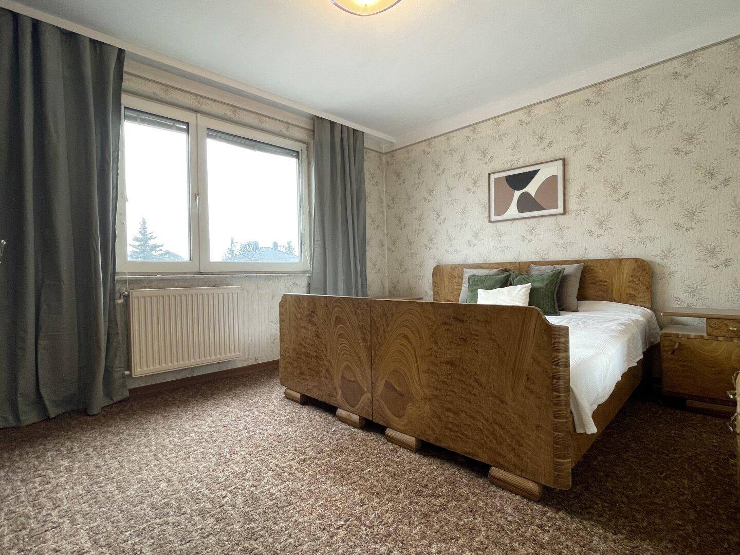 Schlafzimmer mit Teppichboden, großem Holzbett und Fenster mit Blick nach draußen.