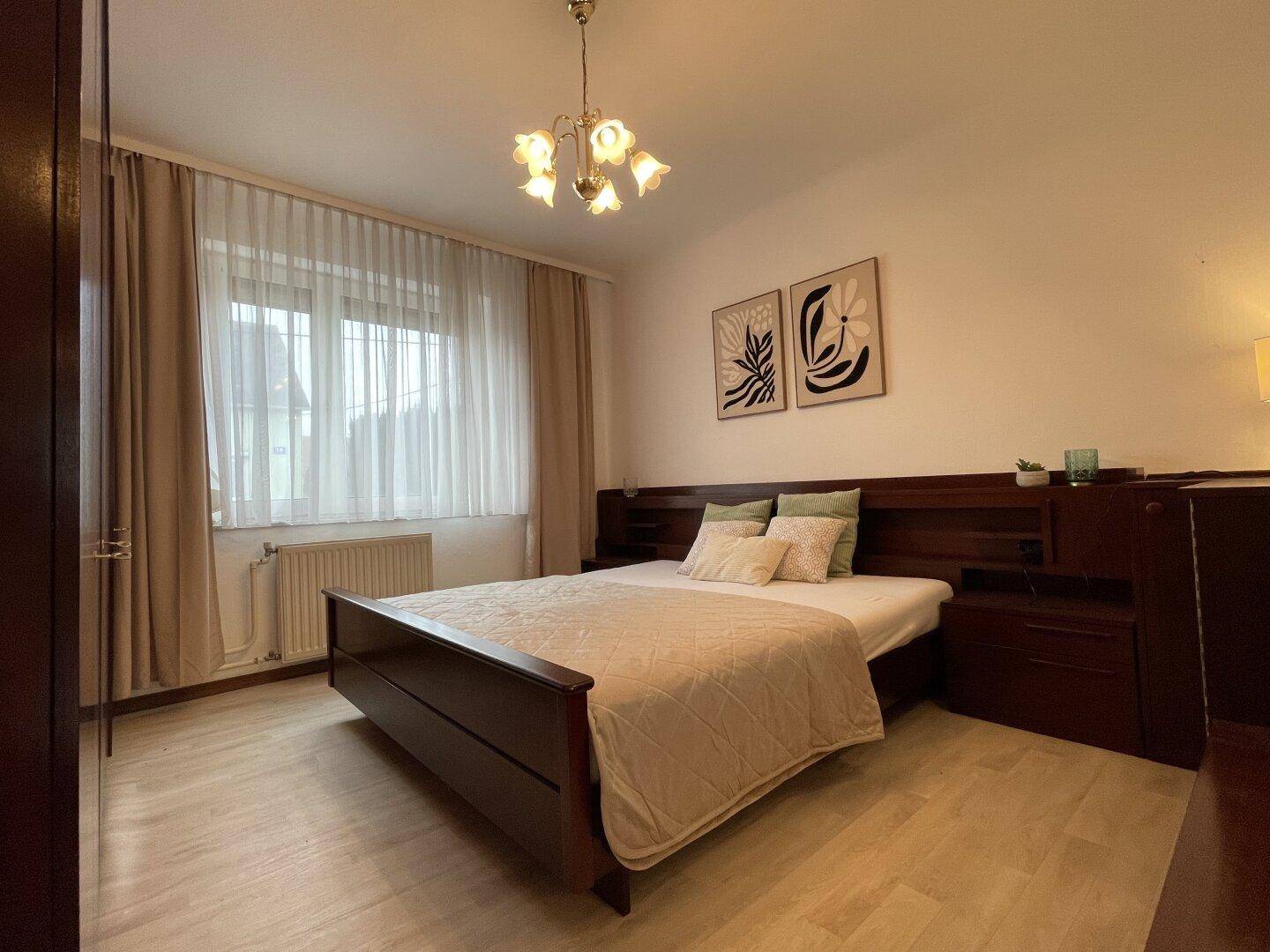 Schlafzimmer mit Holzbett, Parkettboden und Fenster mit Vorhängen.