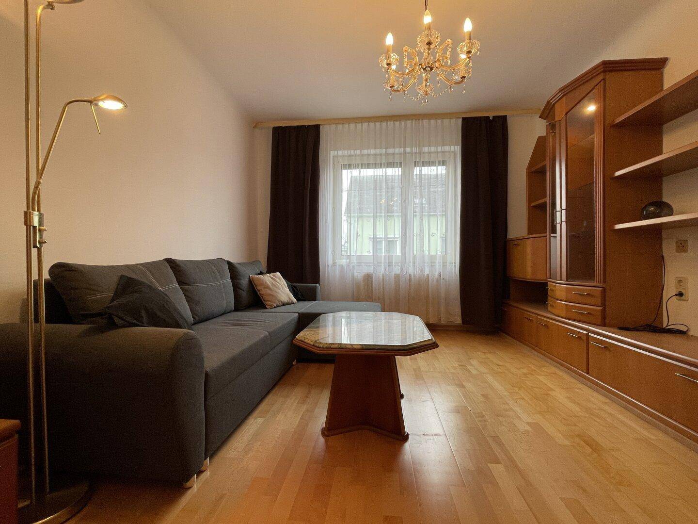 Helles Wohnzimmer mit Parkettboden, bequemer Couch und klassischem Kronleuchter.