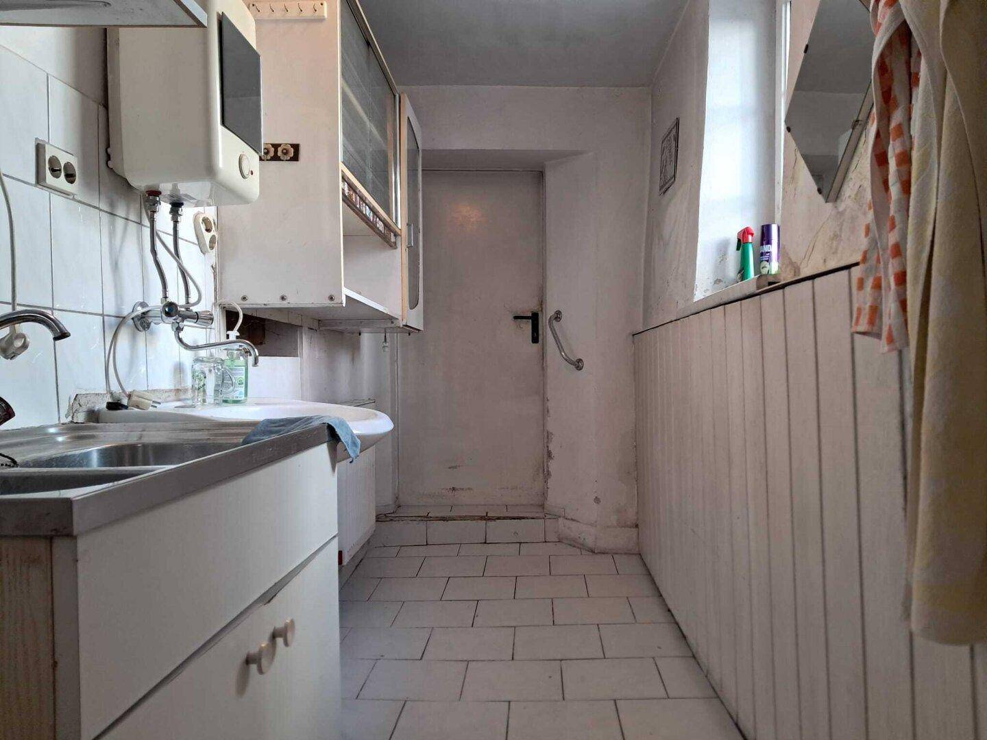 Schmale Küche mit weißen Fliesen, Spülbecken und einem Fenster für Tageslicht.