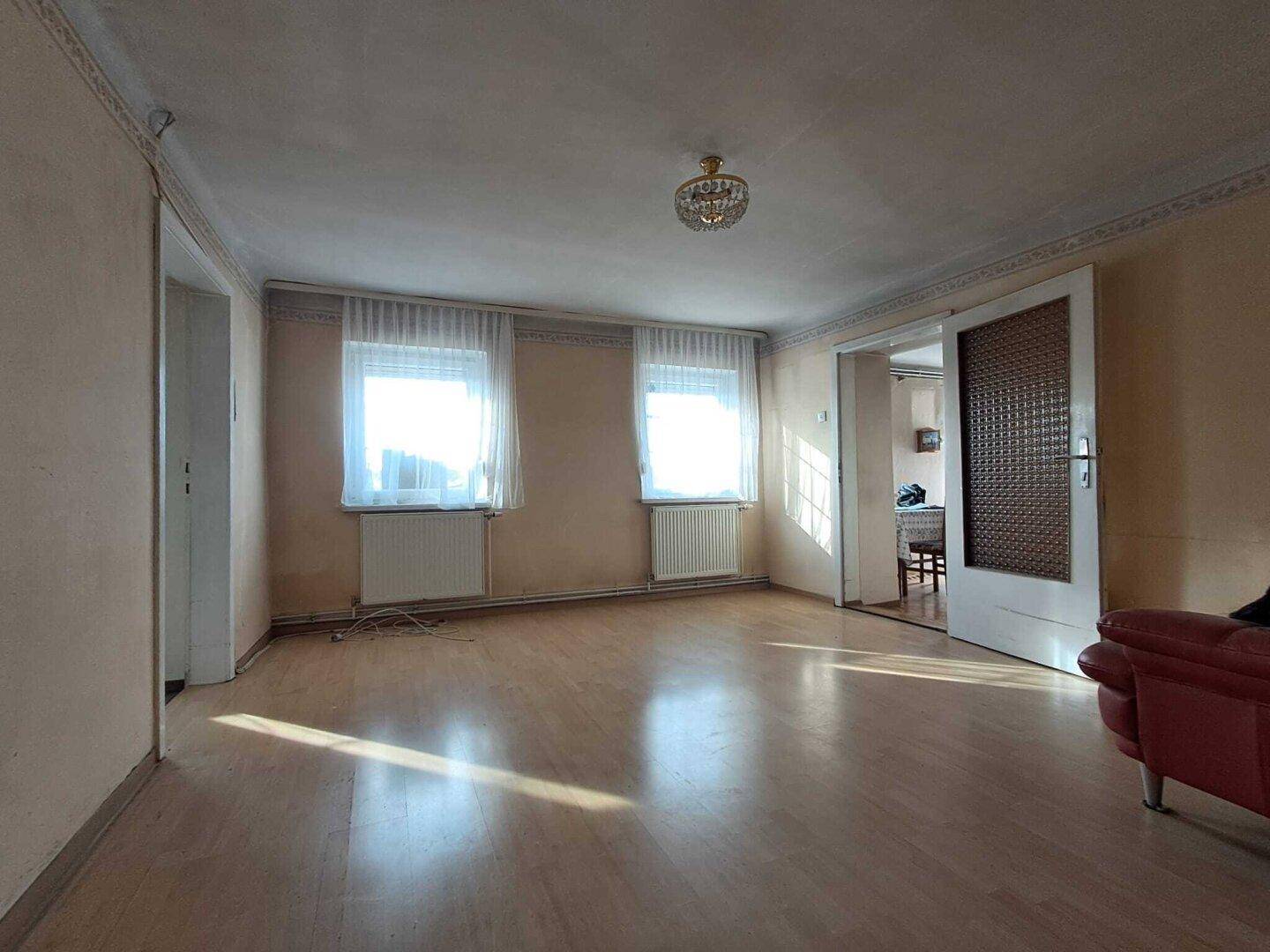 Geräumiges Zimmer mit Laminatboden, zwei Fenstern und Zugang zu einem weiteren Raum.
