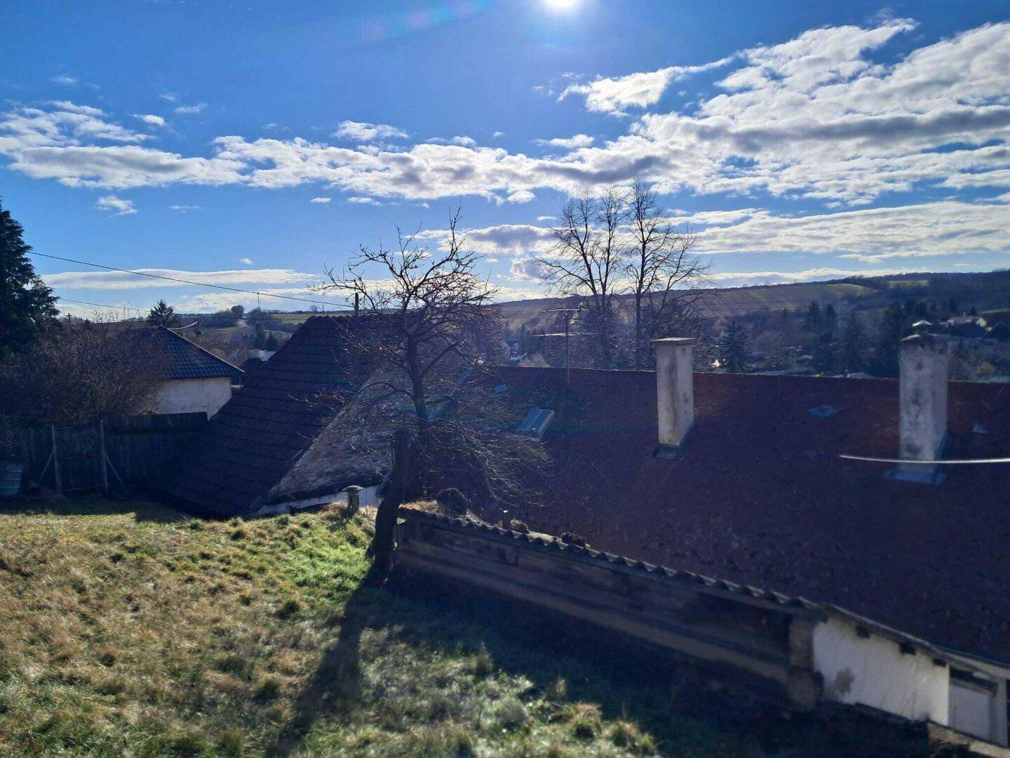 Blick über Dächer und eine hügelige Landschaft unter blauem Himmel mit Wolken.