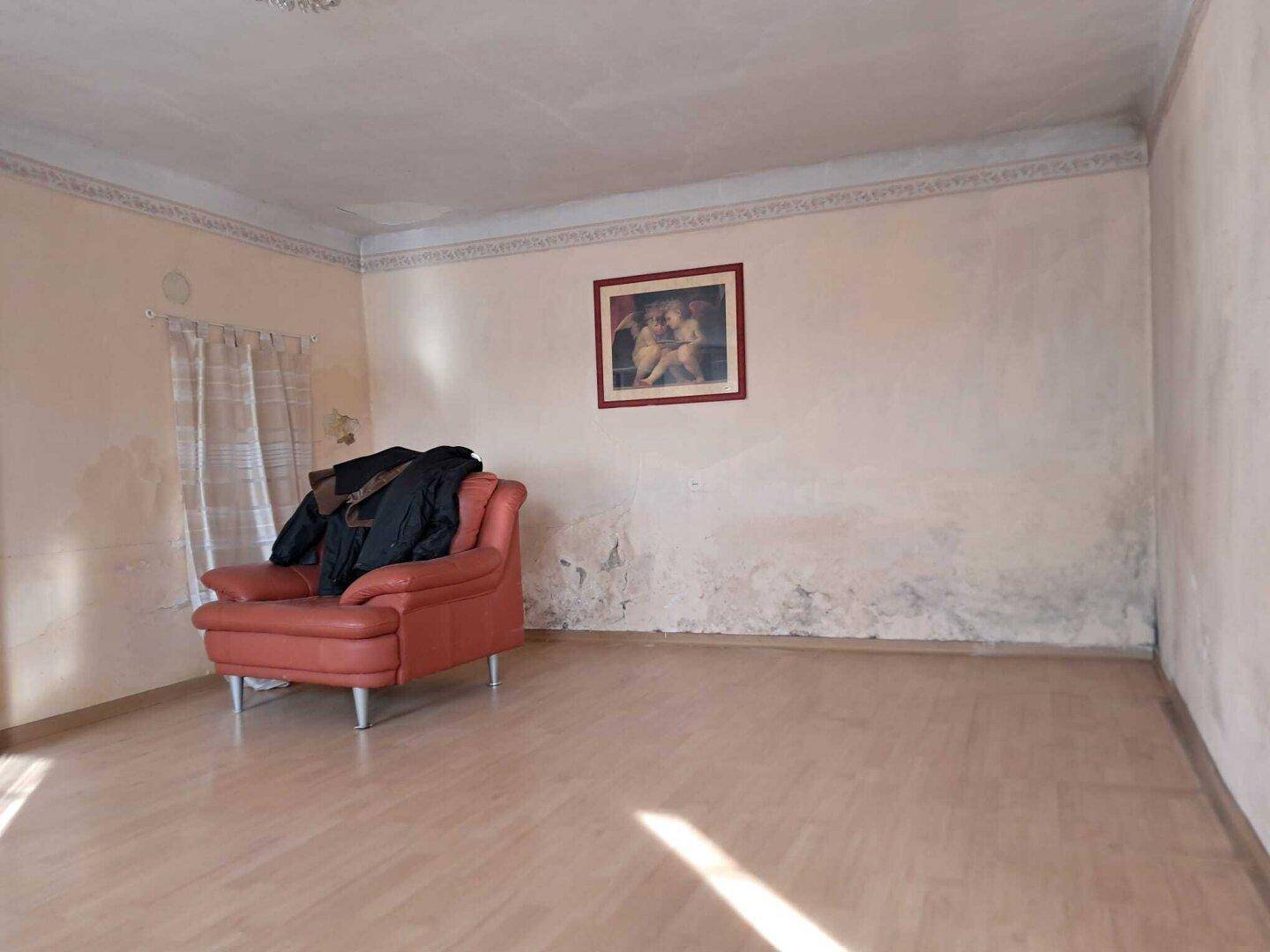 Heller Wohnraum mit Laminatboden und einem roten Sessel, Wände zeigen Abnutzungsspuren.