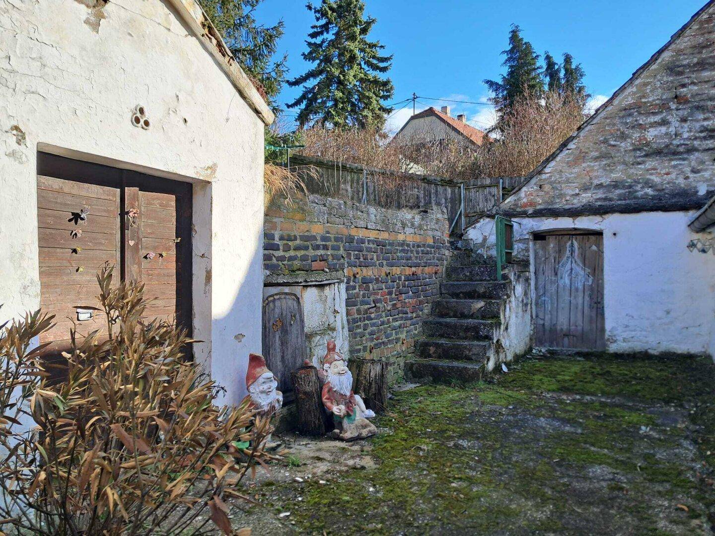 Alter Hof mit Gartenmauern, Treppe und dekorativen Gartenzwergen in ländlicher Umgebung.