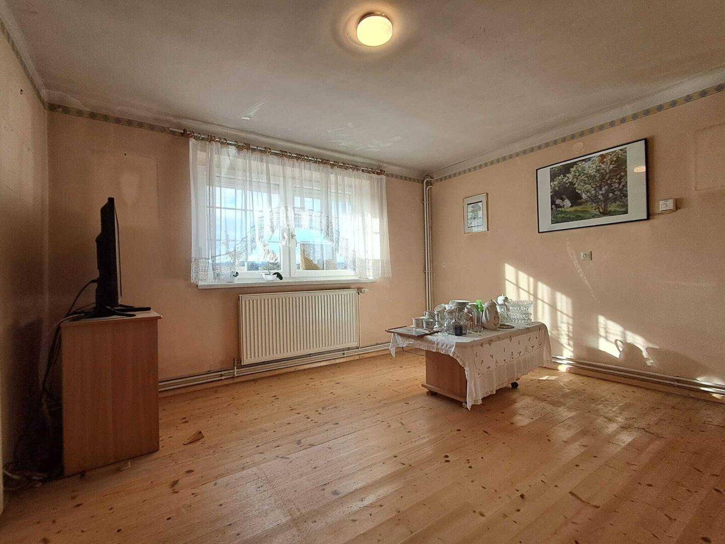 Helles Zimmer mit Holzdielenboden, Heizkörper und einem kleinen Tisch mit Geschirr.