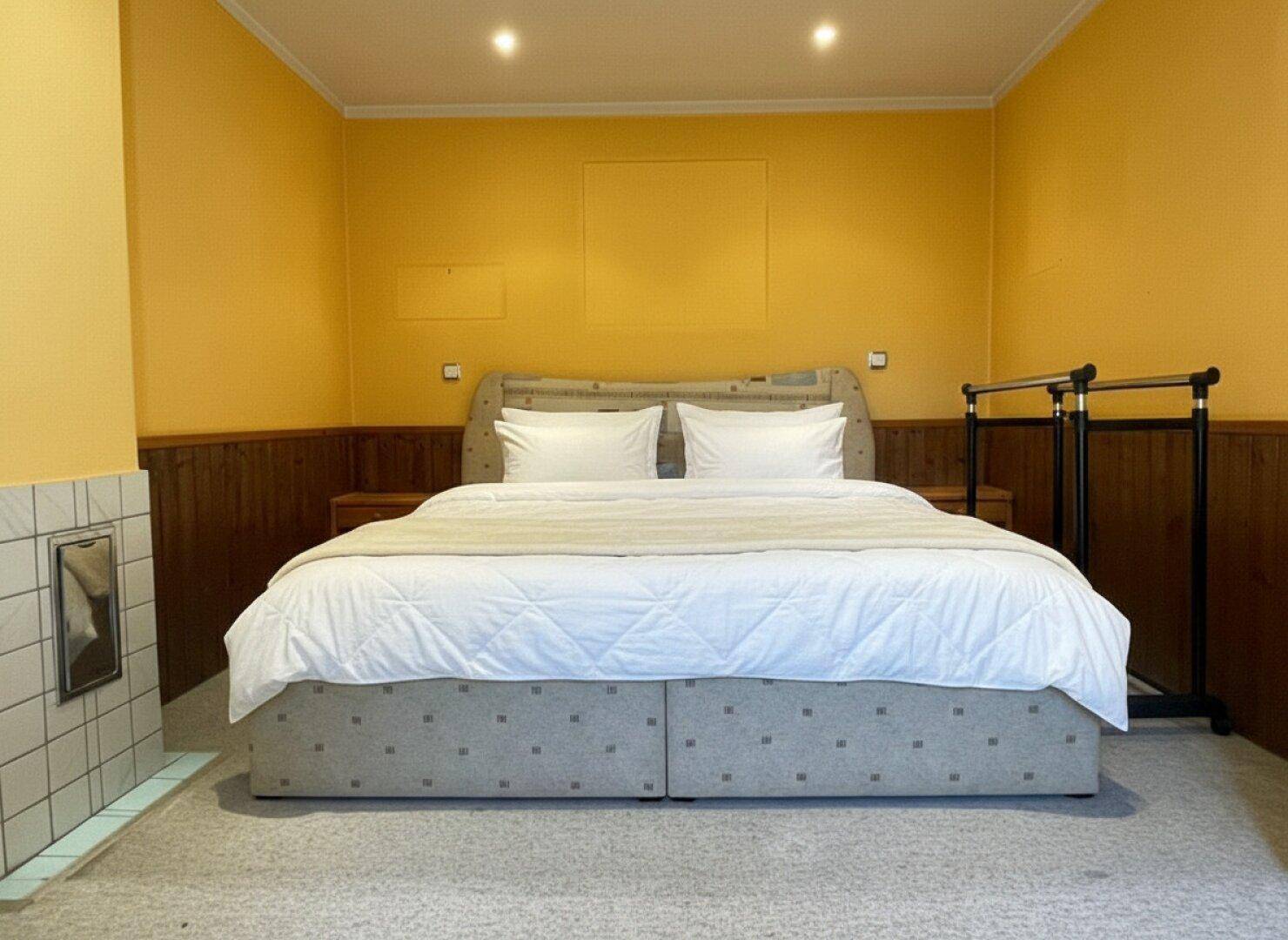 Schlafzimmer mit Doppelbett, Teppichboden und gelben Wänden, die eine warme Atmosphäre schaffen.