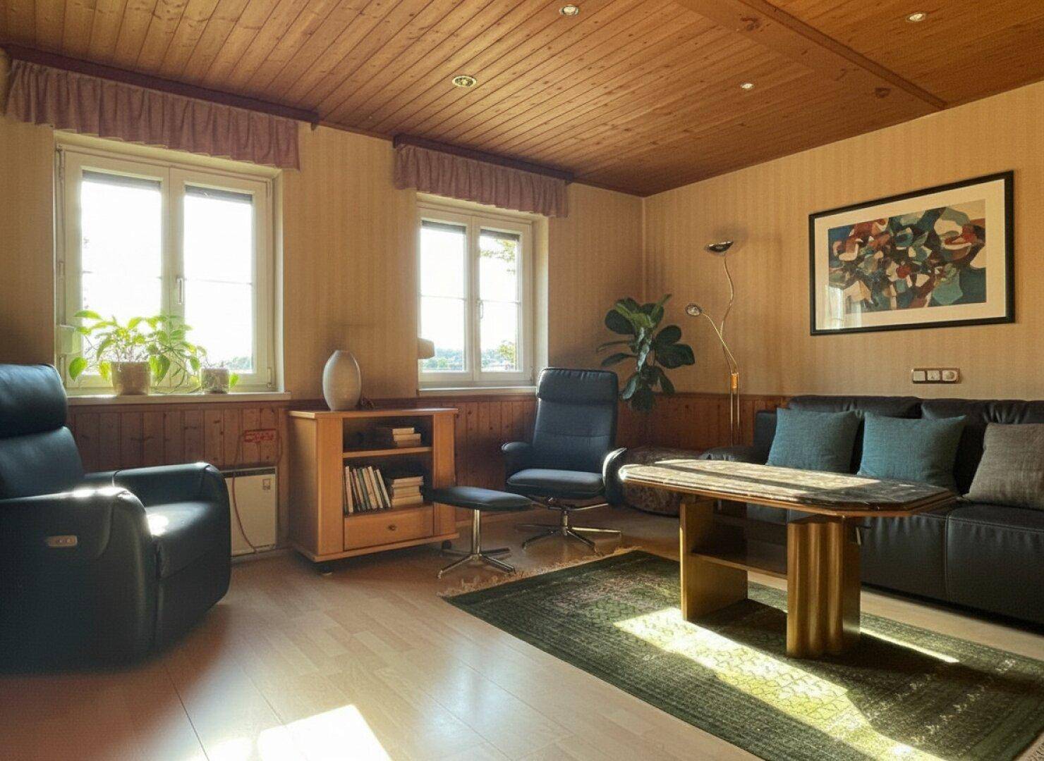 Helles Wohnzimmer mit Holzbalkendecke, Parkettboden und bequemen Ledersesseln.