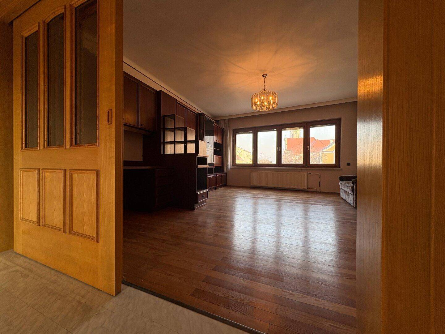 Geräumiges Wohnzimmer mit Holzboden, Kronleuchter und großen Fenstern für viel Tageslicht.