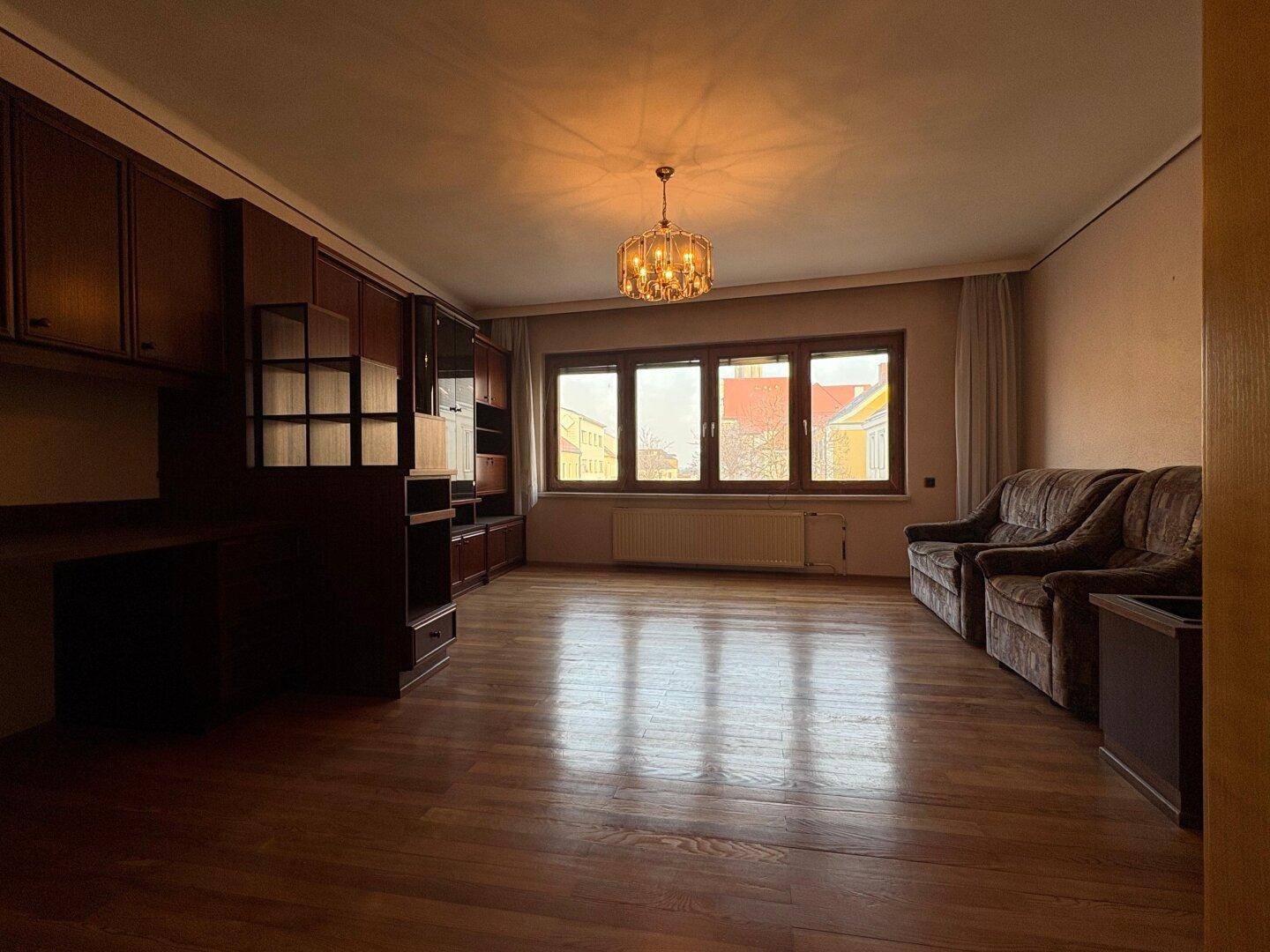 Helles Wohnzimmer mit Parkettboden, bequemen Sofas und einem eleganten Kronleuchter.