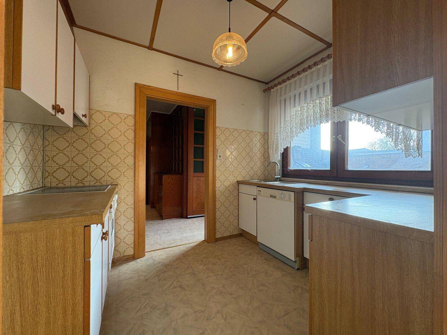 Küche im traditionellen Stil mit älteren Einbauschränken, Spülmaschine und Fenster.