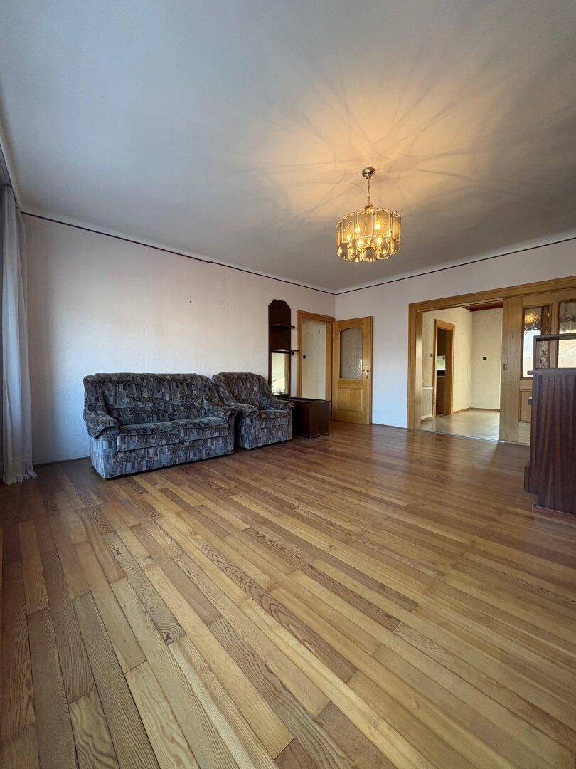 Weitläufiges Wohnzimmer mit glänzendem Holzboden und Zugang zu angrenzenden Räumen.