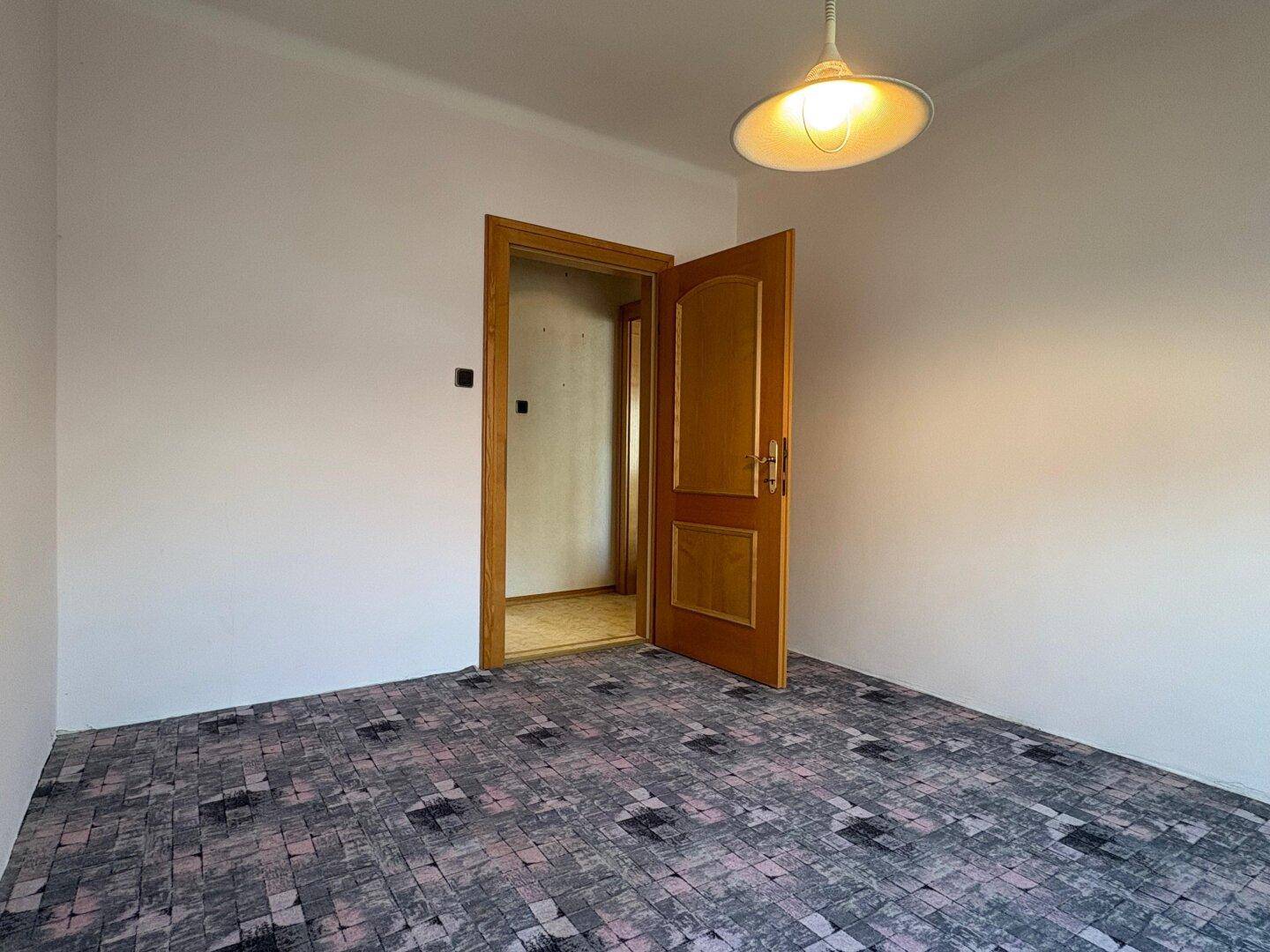 Schlafzimmer mit gemustertem Teppichboden und einer Holztür, die zu einem anderen Raum führt.