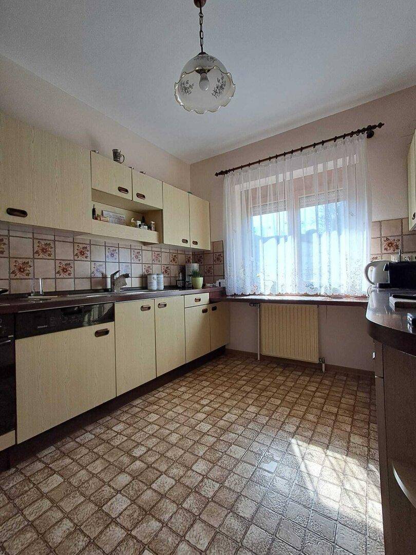 Küche im traditionellen Stil mit gemusterten Fliesen, beigen Schränken und einem Fenster über der Spüle.
