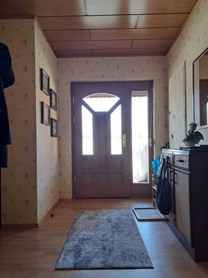Heller Eingangsbereich mit Holztür, Holzdecke und gemusterter Tapete, einladend gestaltet.