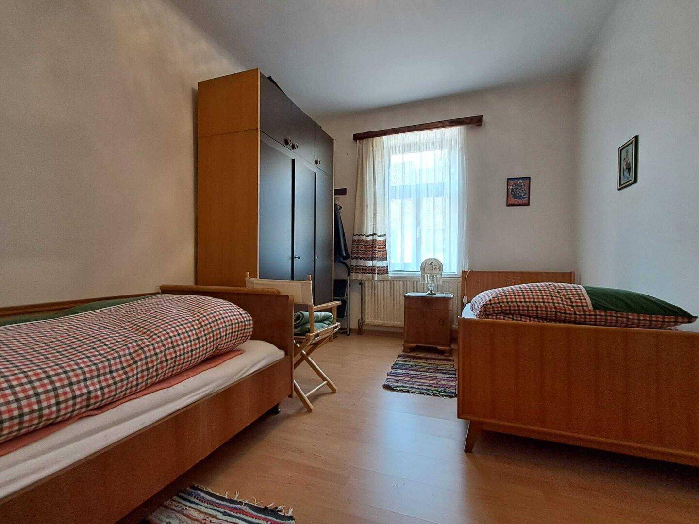 Einfaches Schlafzimmer mit zwei Einzelbetten, Kleiderschrank und Laminatboden.