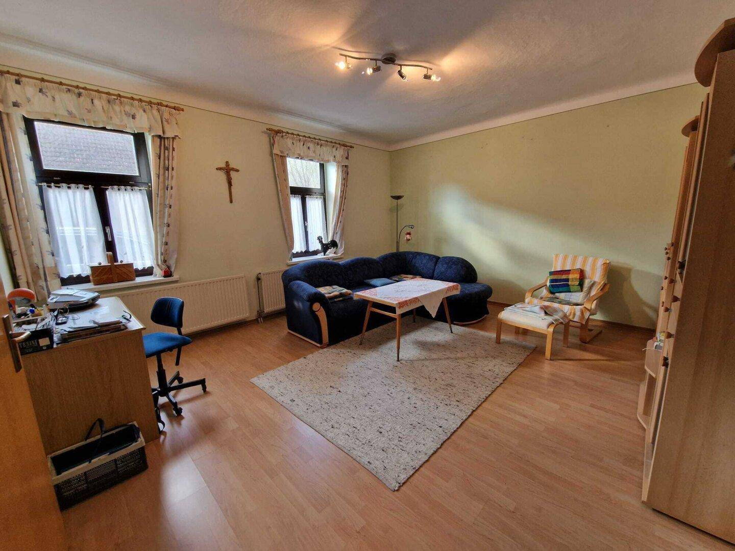 Geräumiges Wohnzimmer mit Laminatboden, traditionellen Möbeln und natürlichem Lichteinfall.