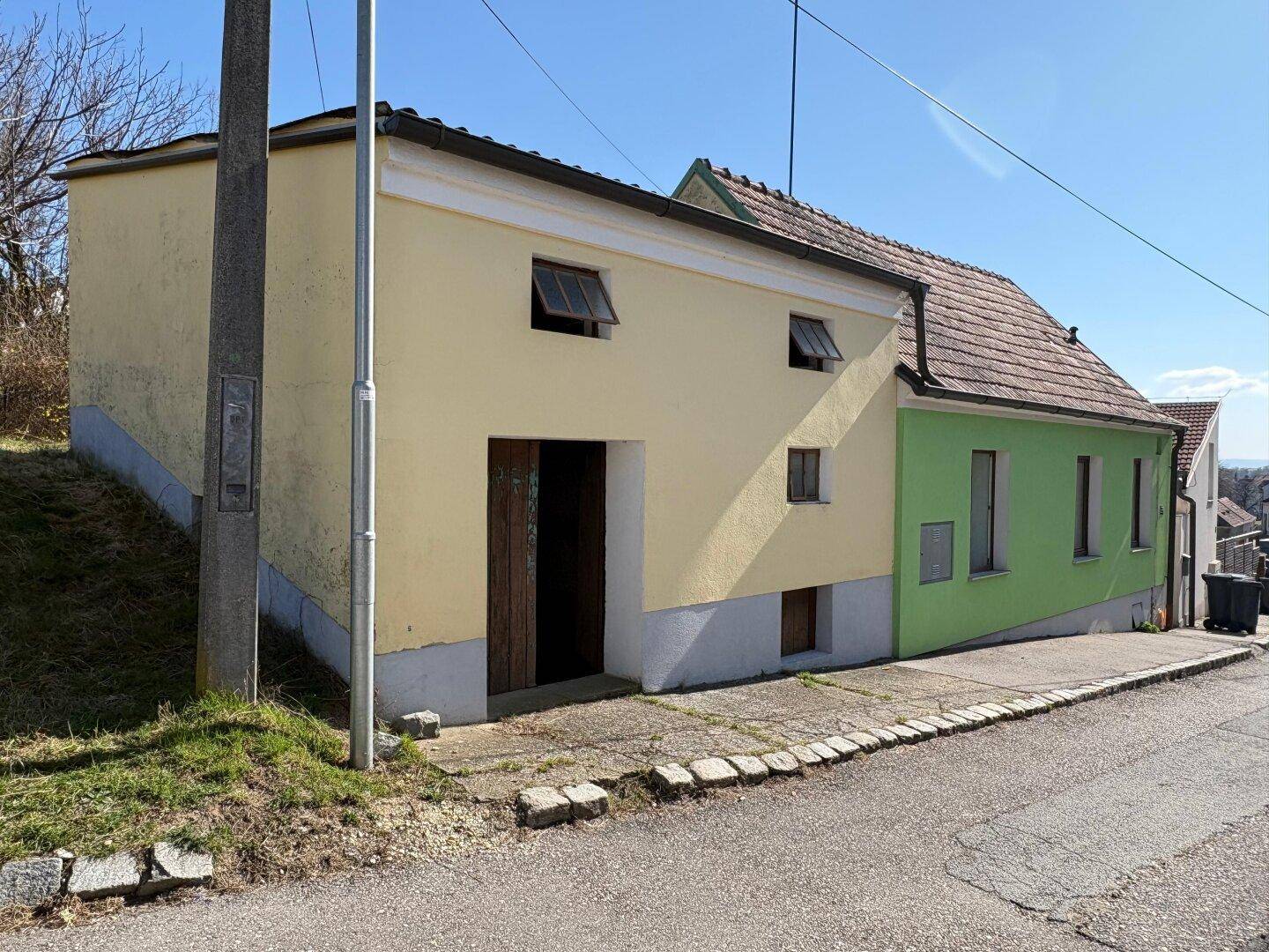 Gelbes und grünes Haus mit schrägem Dach und einfacher Architektur in ländlicher Umgebung.
