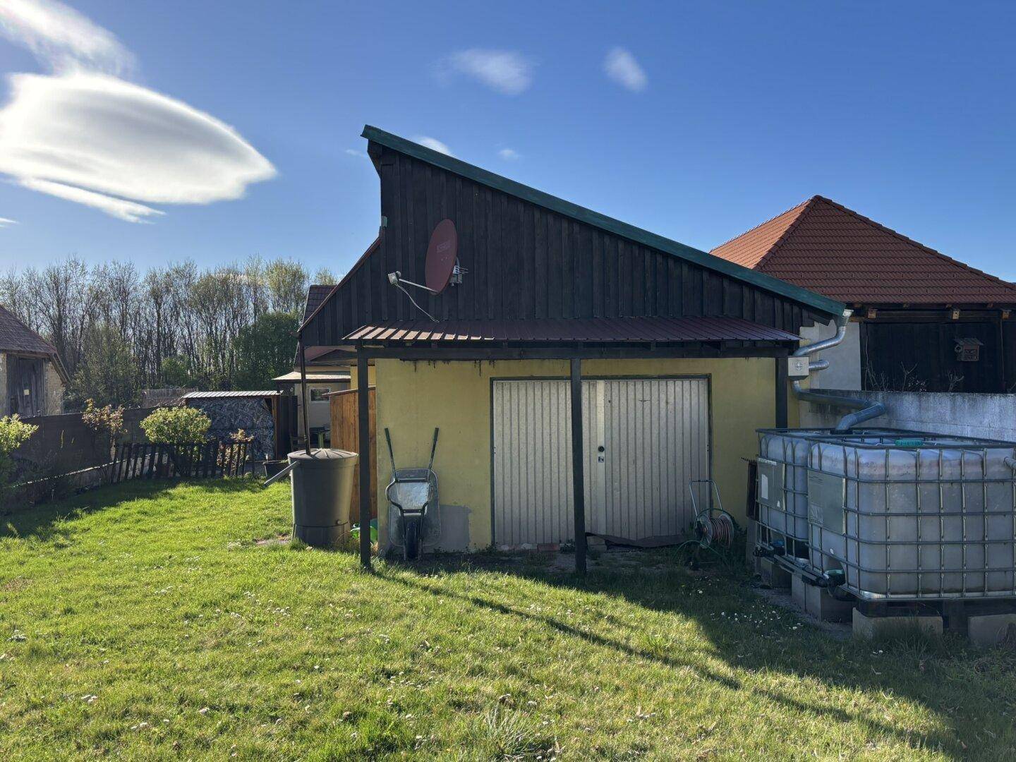 Seitenansicht des Hauses mit Anbau, Garage und großem Garten unter strahlend blauem Himmel.