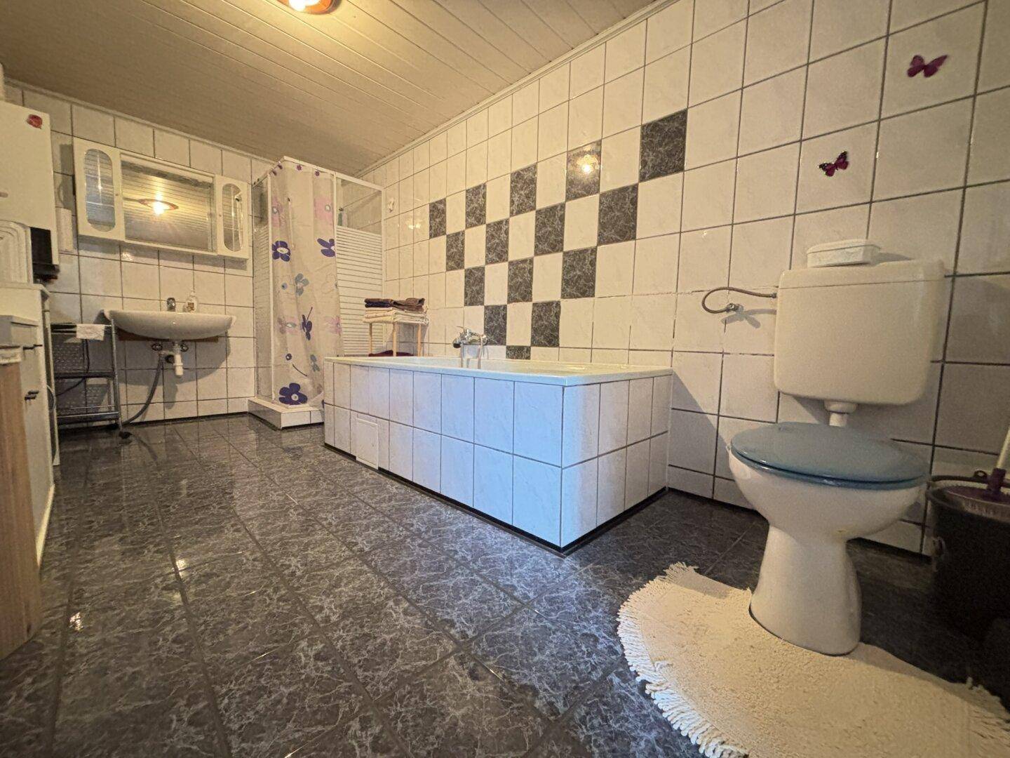 Gefliestes Badezimmer mit Badewanne, Toilette und Waschbecken in einem älteren Stil.