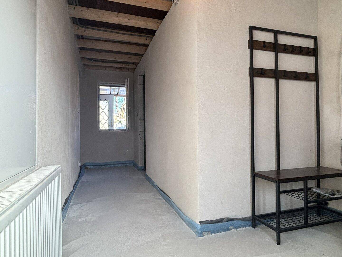 Flur im Rohbauzustand mit sichtbaren Deckenbalken und Betonboden, bereit für den Ausbau.