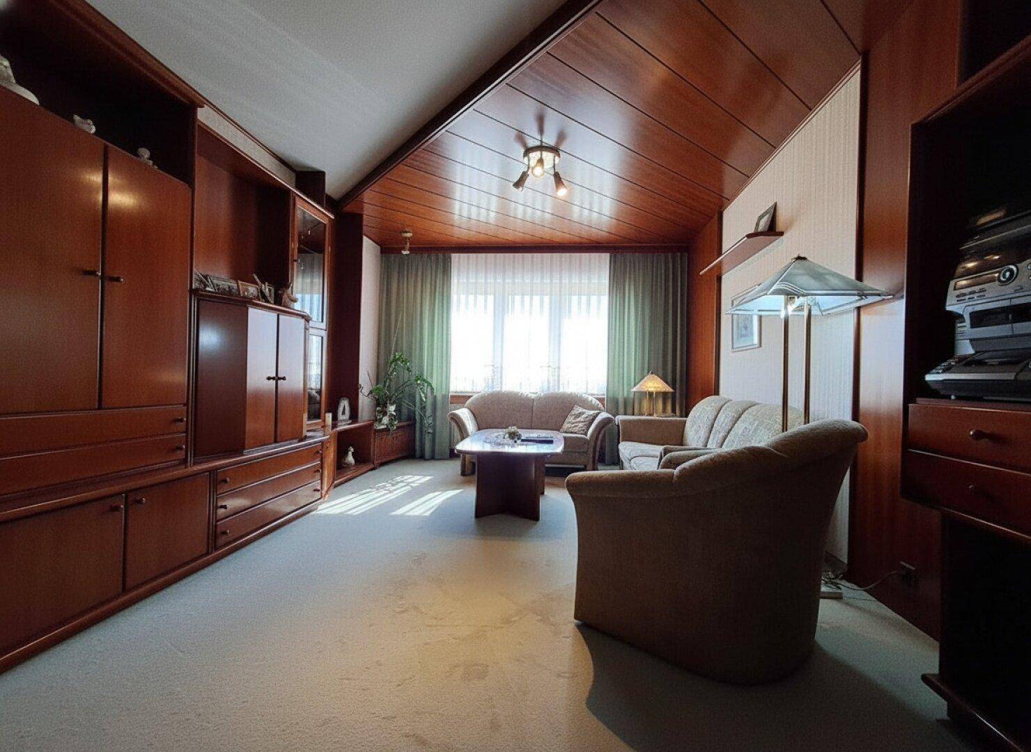 Geräumiges Wohnzimmer mit Holzvertäfelung, Teppichboden und viel Tageslicht.