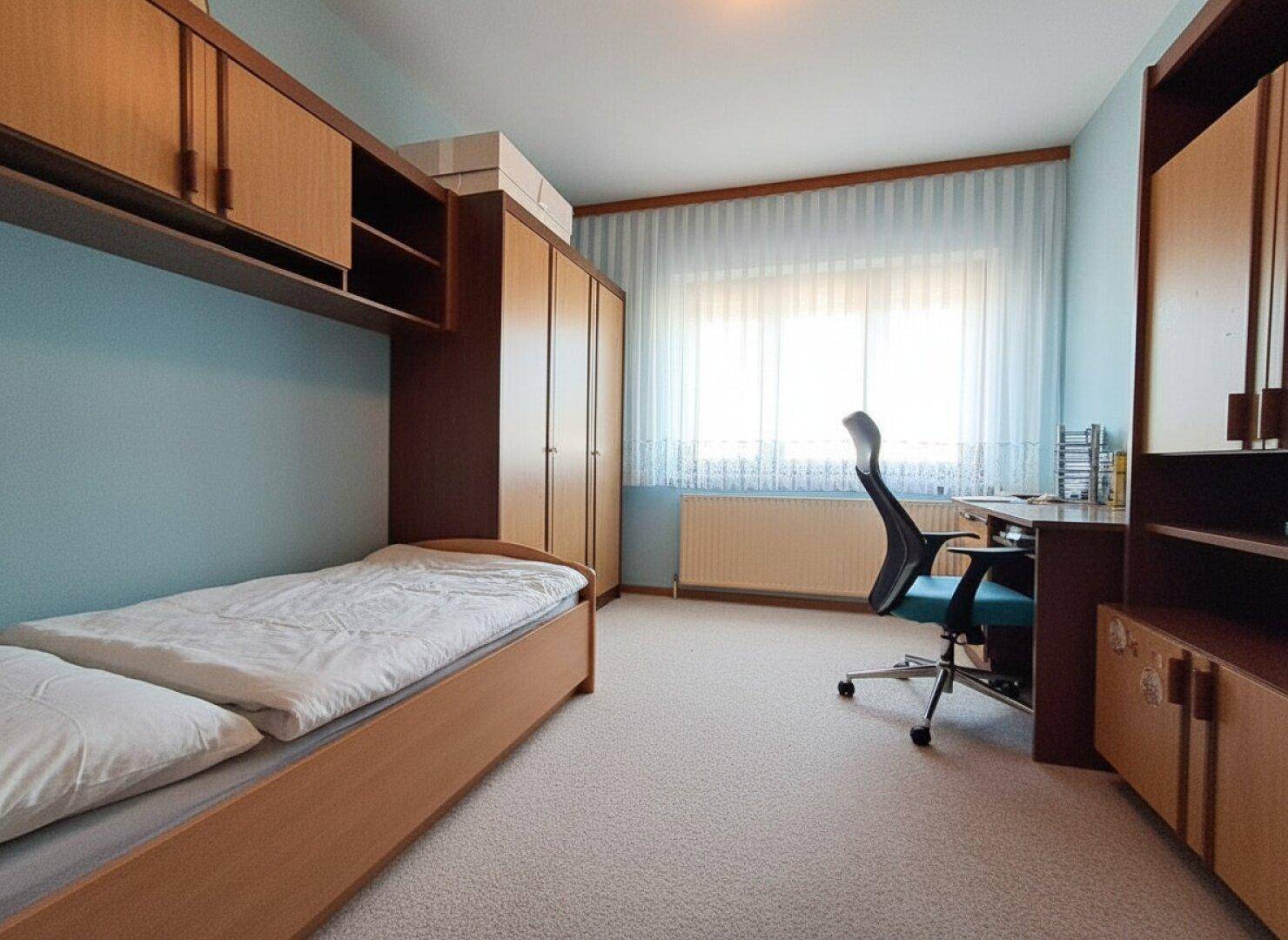 Kinderzimmer oder Gästezimmer mit Schreibtisch, Einbauschränken und Teppichboden.