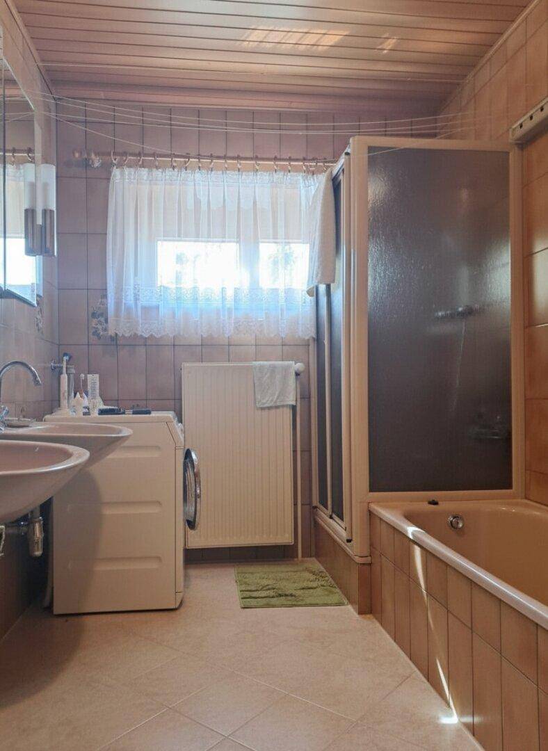 Funktionales Badezimmer mit Badewanne, Dusche, Doppelwaschbecken und Fenster.