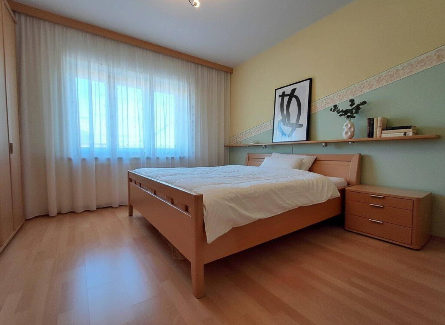 Helles Schlafzimmer mit Holzfußboden, großem Fenster und moderner Wandgestaltung.