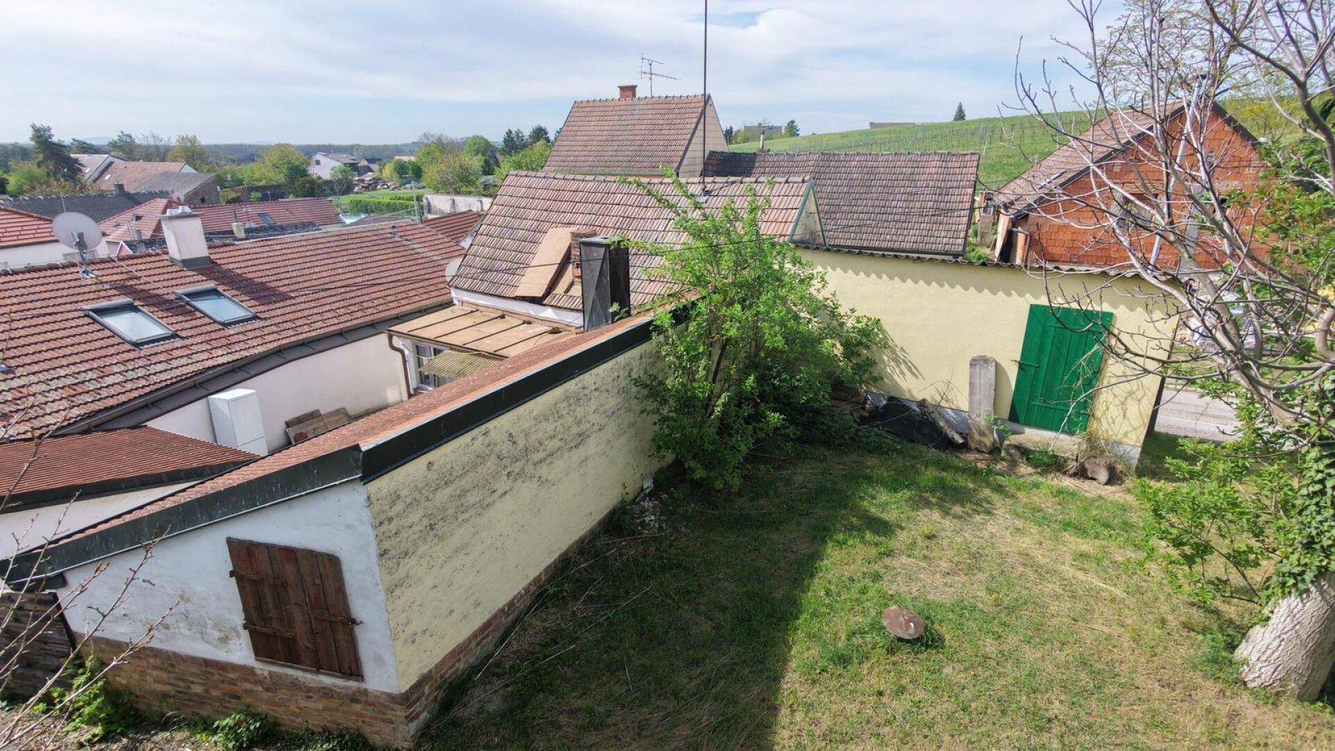 Blick von oben auf die Rückseite der Gebäude mit einem grasbewachsenen Hang und weiteren Dächern in der Umgebung.