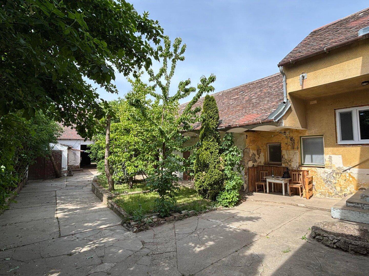 Ein gepflasterter Innenhof mit Grünflächen, Bäumen und einer kleinen Sitzecke vor einem älteren Gebäude.