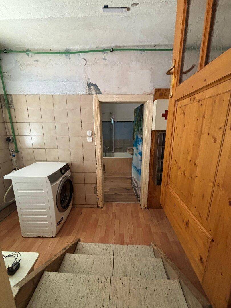 Ein Hauswirtschaftsraum mit Waschmaschine und gefliesten Wänden, der zum Badezimmer führt.