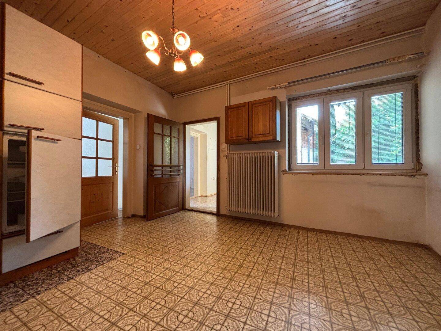 Geräumige Küche mit Holzdecke, Fenster und Heizkörper, die auf eine Renovierung wartet.