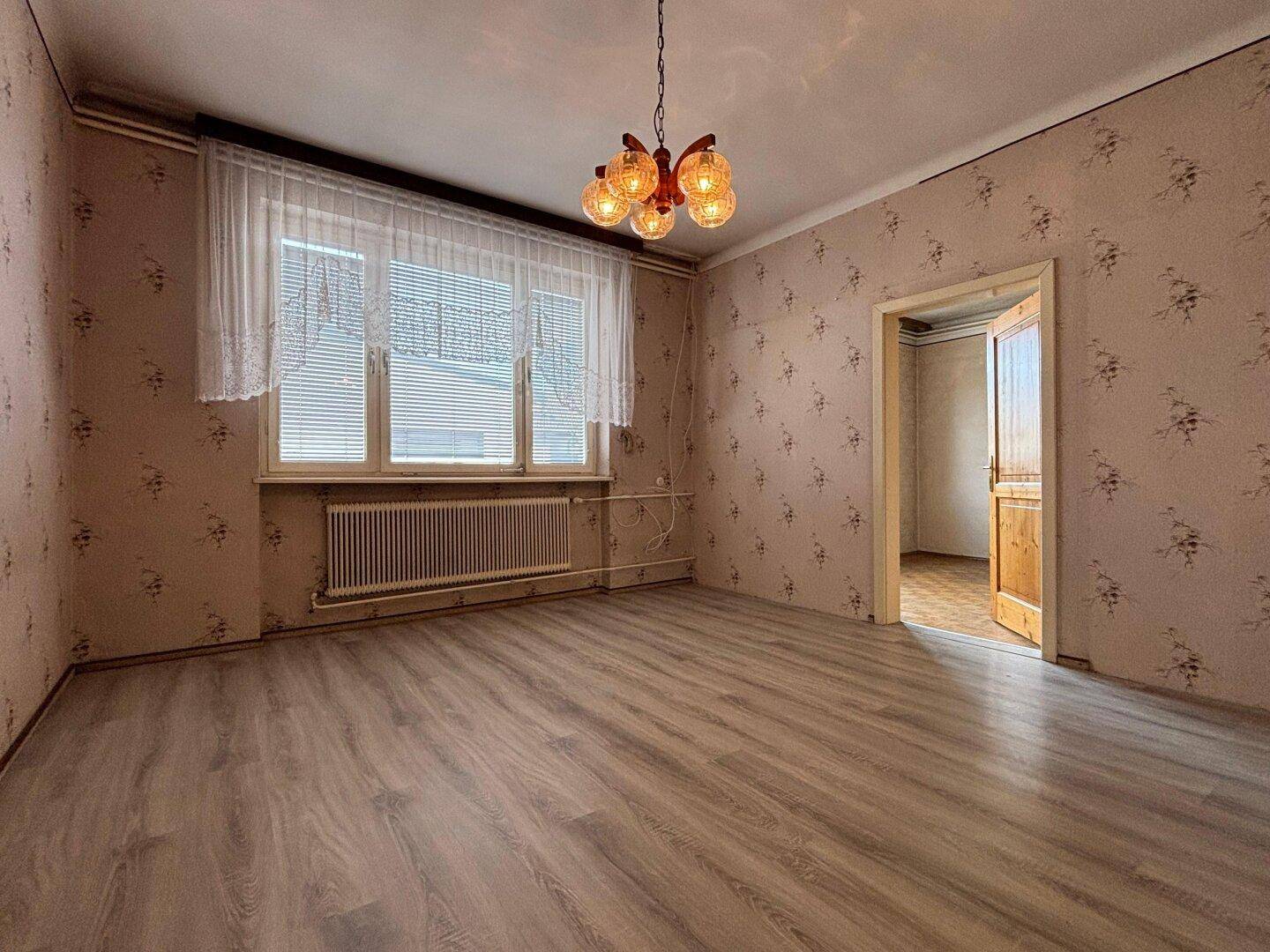 Ein Zimmer mit Laminatboden und floraler Tapete, das auf eine Modernisierung wartet.