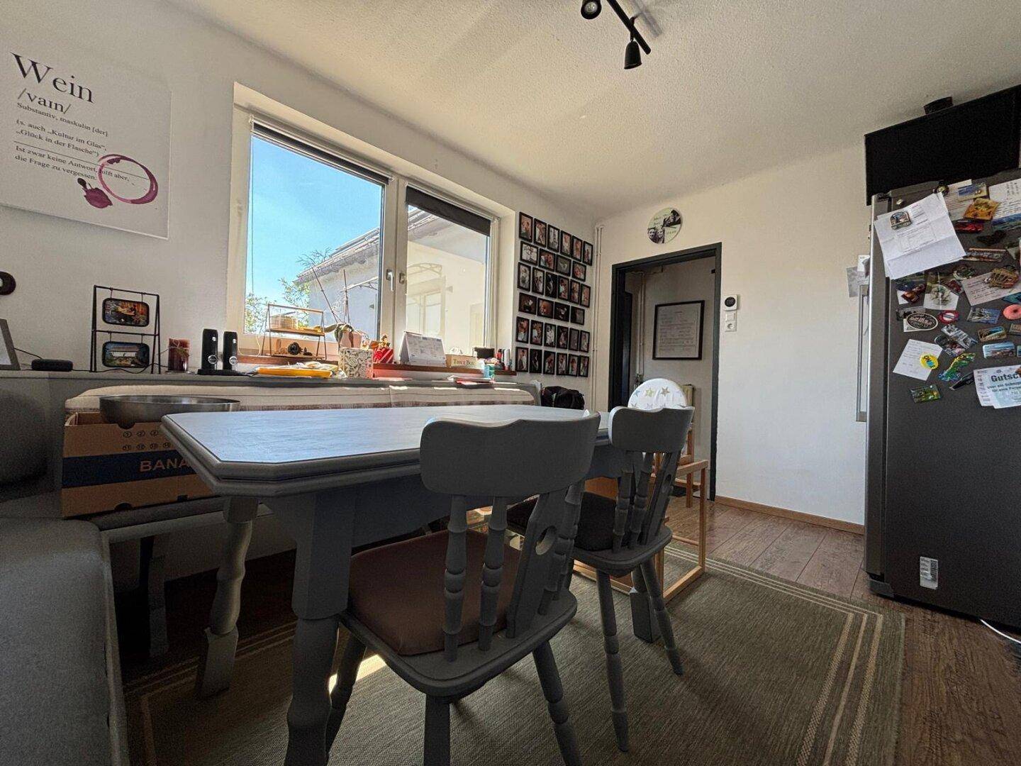 Essbereich in der Küche mit Esstisch, Stühlen und Kühlschrank neben einem Fenster.