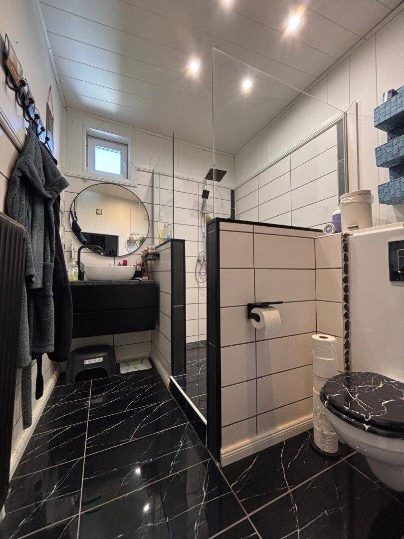 Modernes Badezimmer mit schwarzem Marmorfliesenboden, begehbarer Dusche und Fenster.