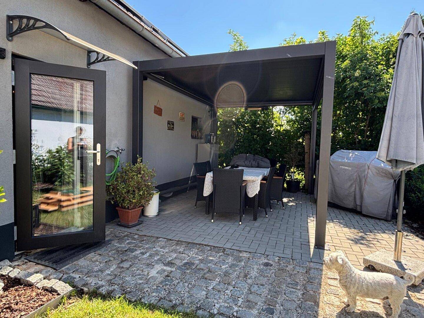Überdachte Terrasse mit Esstisch und Stühlen, ideal für Mahlzeiten im Freien.