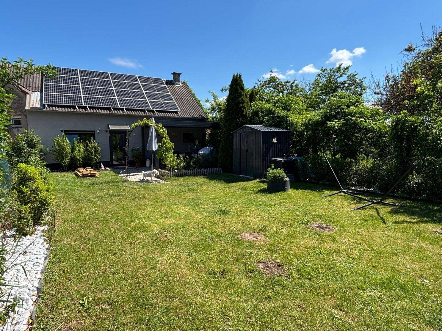 Hinterhof mit Rasenfläche, Gartenhaus und Photovoltaikanlage auf dem Hausdach.