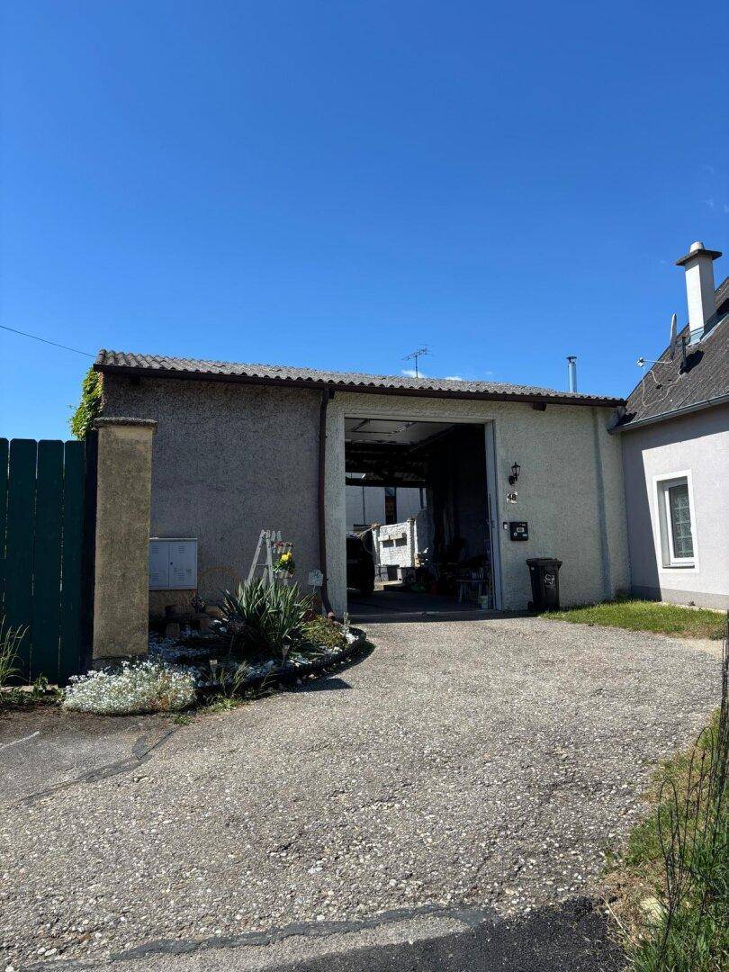 Freistehende Garage mit offenem Tor und Zufahrt auf einem sonnigen Grundstück.