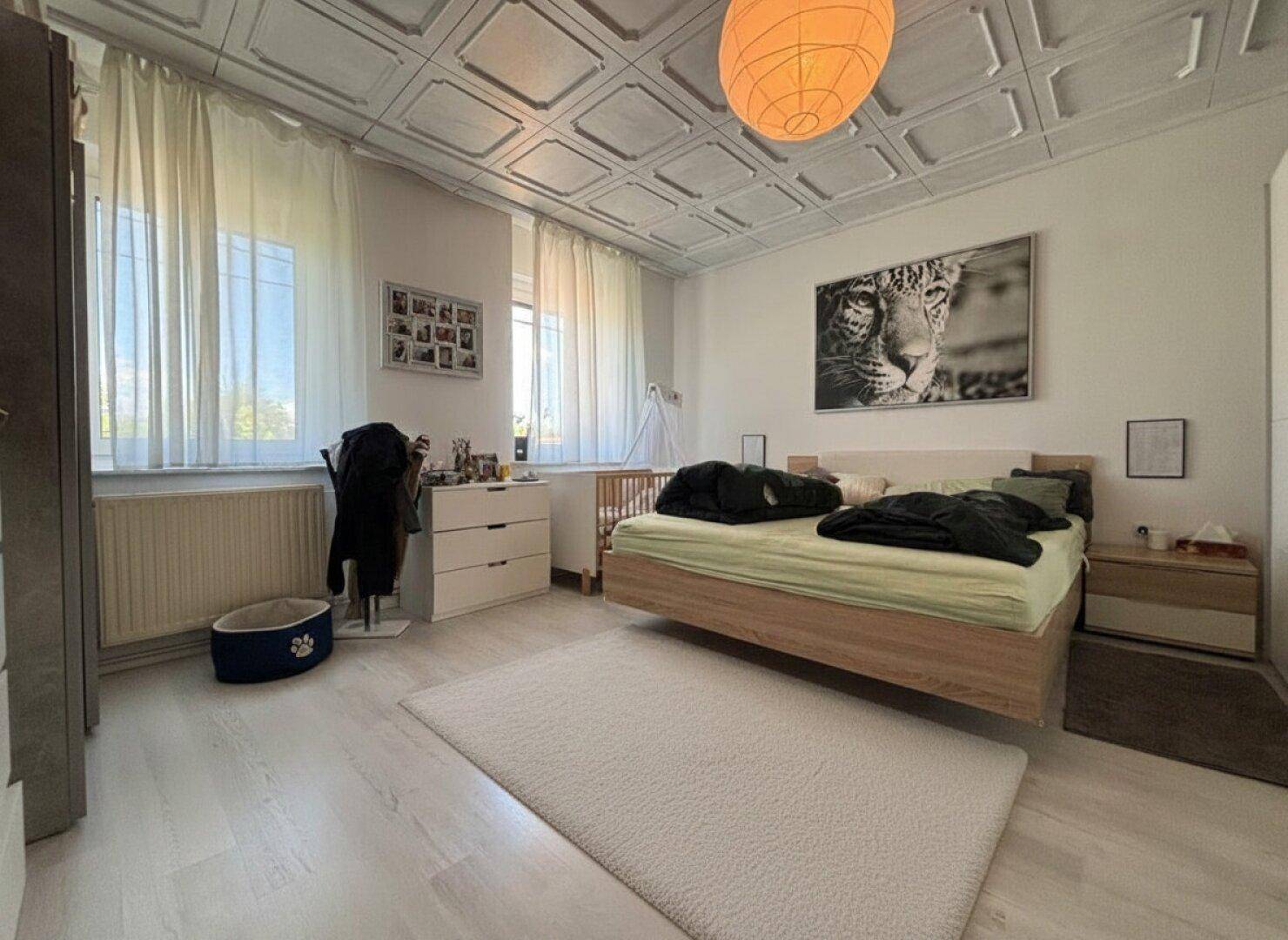 Schlafzimmer mit Doppelbett, hellem Laminatboden und dekorativer Deckenverkleidung.