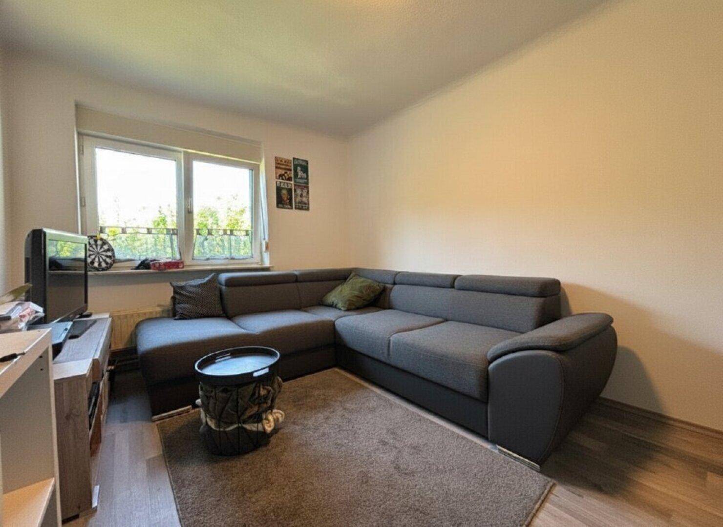 Gemütliches Wohnzimmer mit großem Ecksofa, Teppich und Fenster mit Blick ins Grüne.