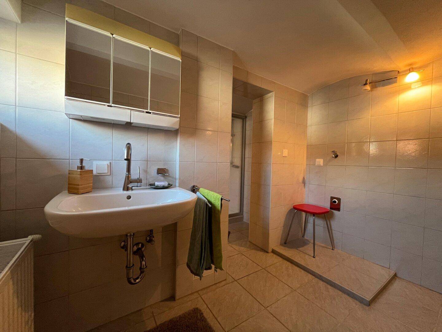 Funktionales Badezimmer mit Fliesen, Waschbecken und Duschbereich mit Sitzgelegenheit.
