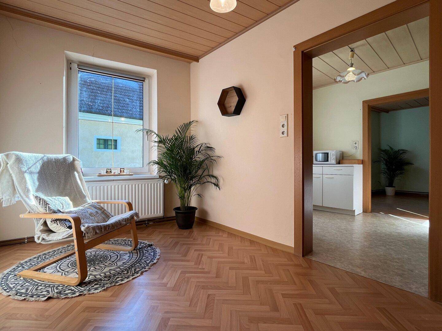 Gemütliches Wohnzimmer mit Holzbalkendecke, Laminatboden und Blick in den Essbereich.
