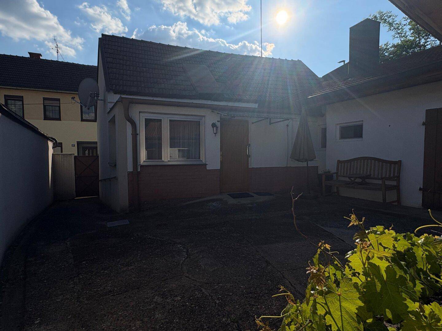 Hausfassade mit Satteldach und einem kleinen, sonnigen Hofbereich mit Sitzbank.