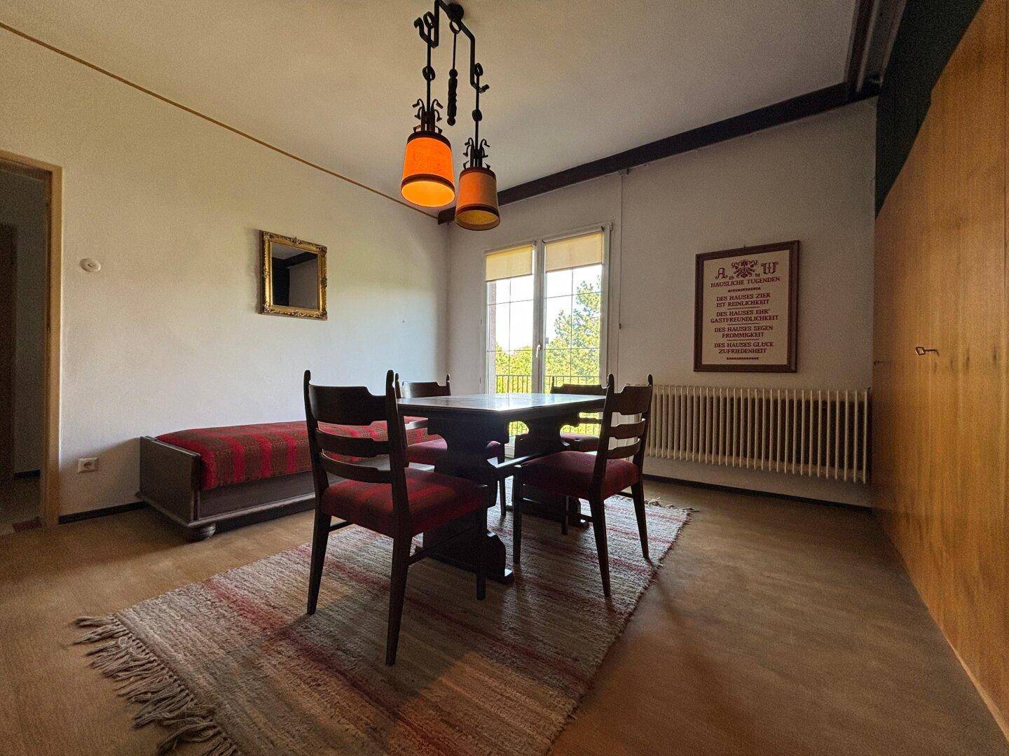 Wohnbereich mit Holzbalken, Esstisch und Zugang zu einem Balkon mit Aussicht.