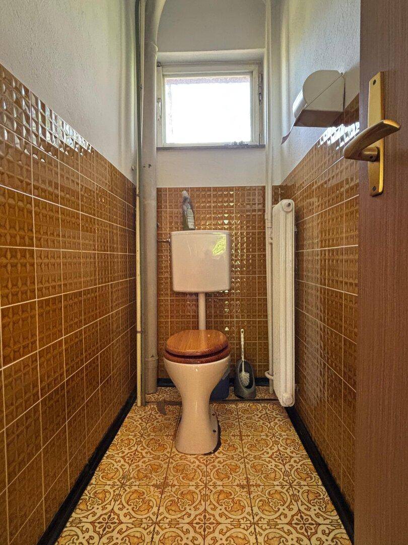 Kleines Gäste-WC mit braunen Fliesen, Fenster und traditioneller Toilette.