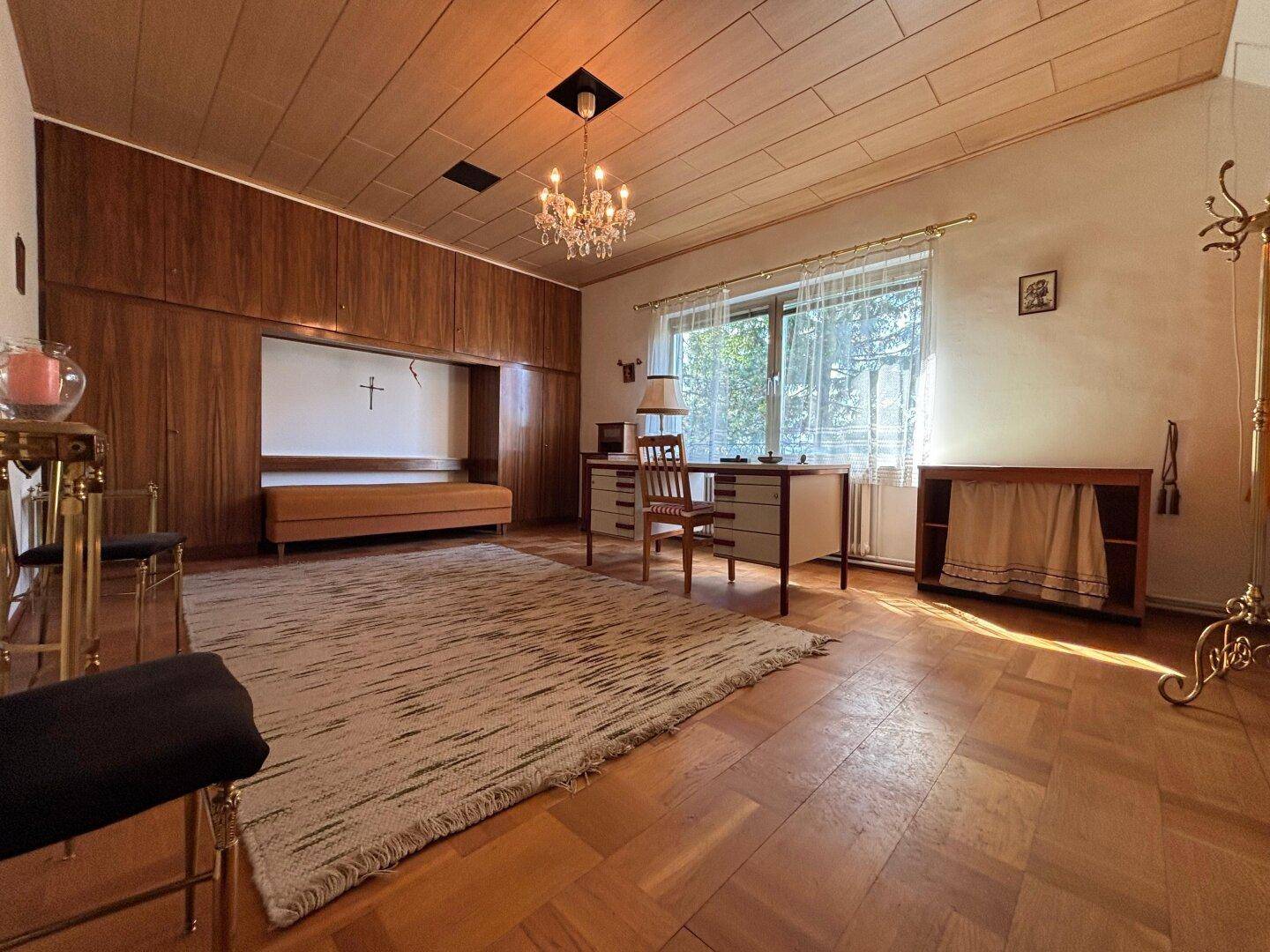 Helles Arbeitszimmer mit Parkettboden, Holzvertäfelung und Blick ins Grüne.