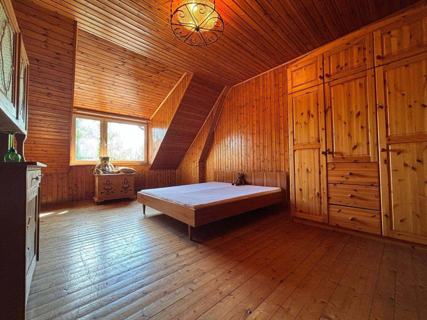 Rustikales Schlafzimmer im Dachgeschoss mit Holzvertäfelung, Holzboden und Dachschräge.