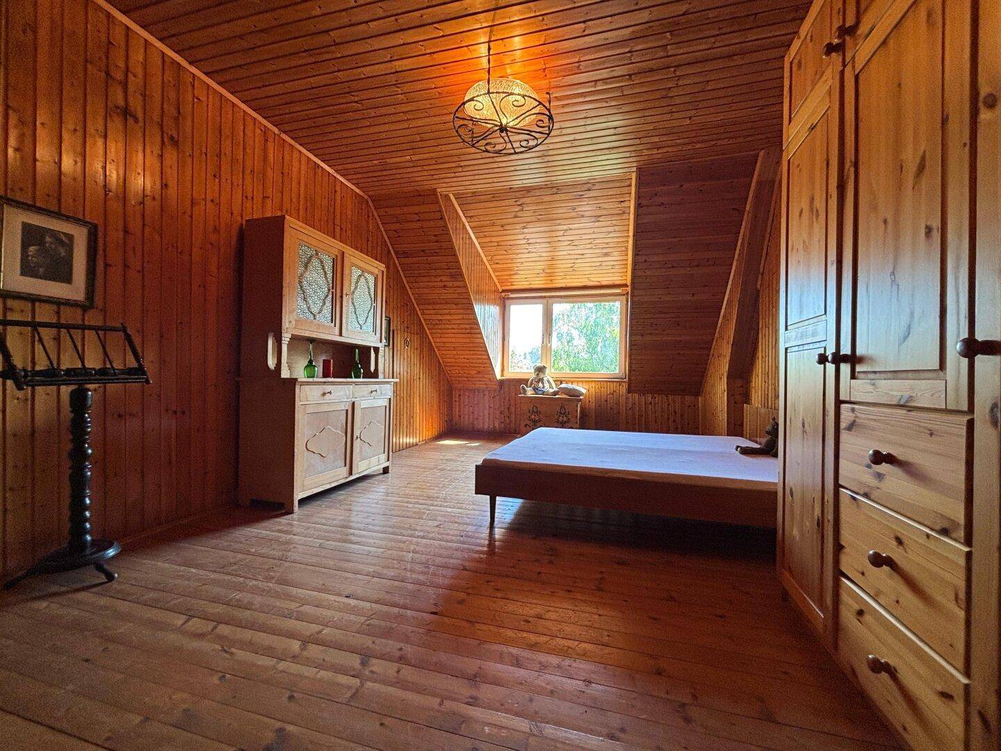 Gemütliches Schlafzimmer im Dachgeschoss mit Holzvertäfelung, Holzboden und Dachschräge.