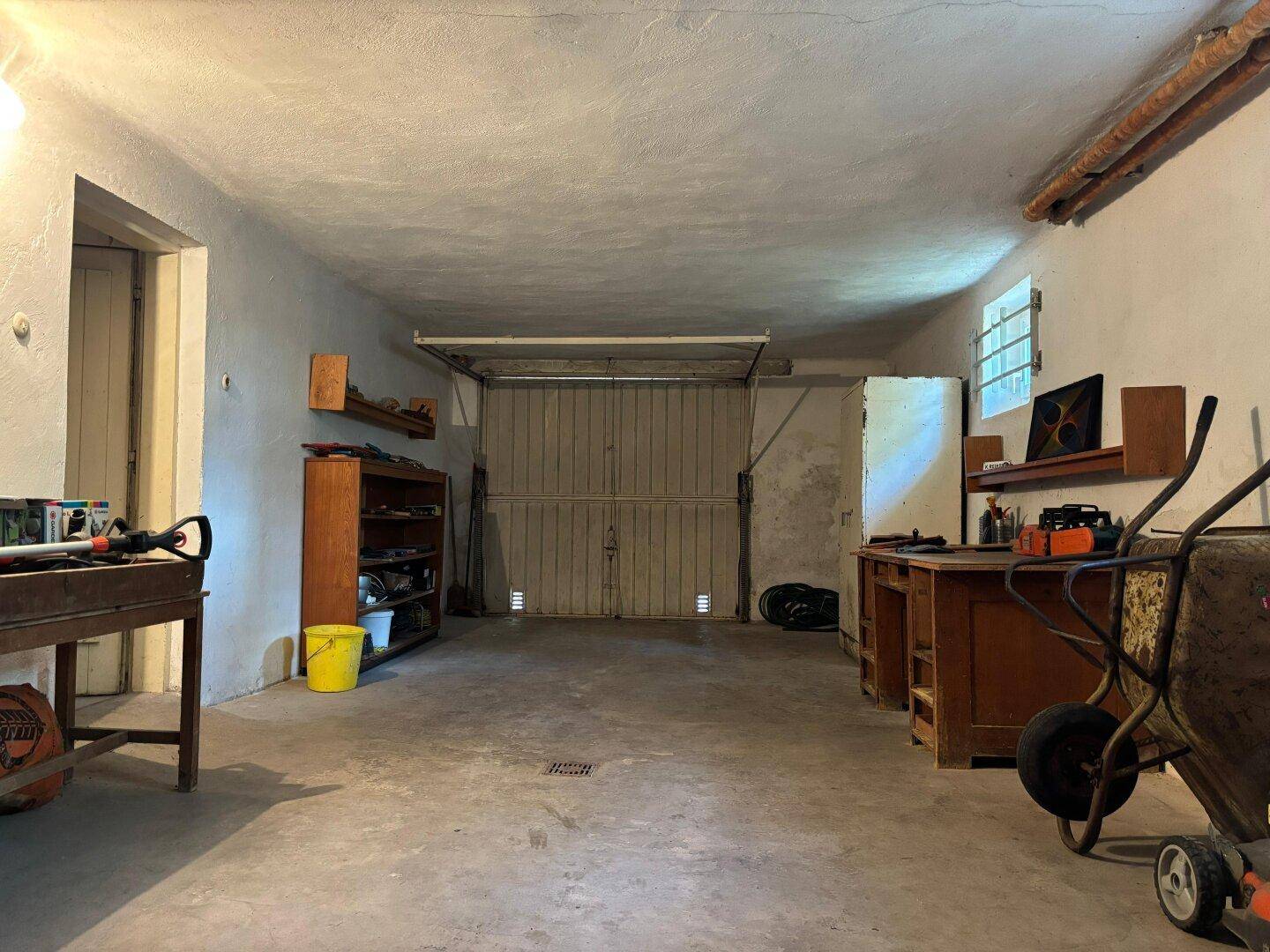 Geräumige Garage mit Betonboden und Platz für Werkzeuge und Fahrzeuge.